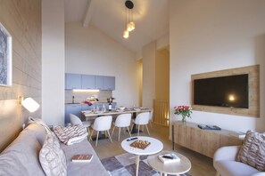 Ein modernes Wohnzimmer mit einer Couch, einem Couchtisch, einem an der Wand befestigten Fernseher und einem Essbereich mit Stühlen und einem Tisch.