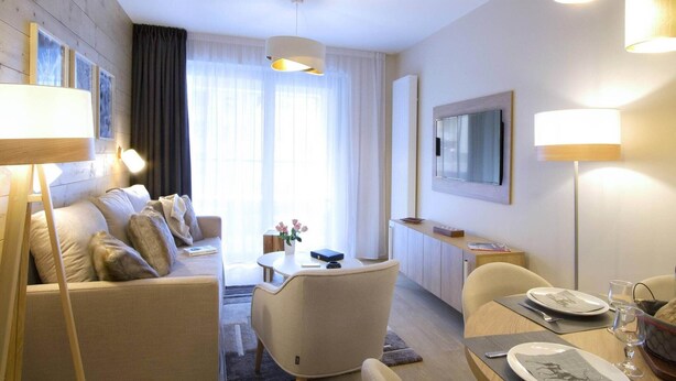 Une chambre d’hôtel équipée d’un canapé, d’un fauteuil, d’une table à manger et d’un téléviseur fixé au mur.