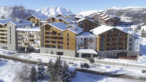 Une station de montagne enneigée, avec des bâtiments à plusieurs étages, des remontées mécaniques et une vue dégagée sur les montagnes.