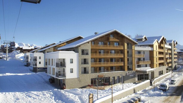 Et hotel med flere etager og et skihejs i baggrunden, omgivet af sne.