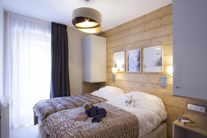 A hotel room with two beds, a large window with curtains, a wall-mounted light fixture, and framed pictures. - Apartment in L'Éclose with Mountain Views (Huez)