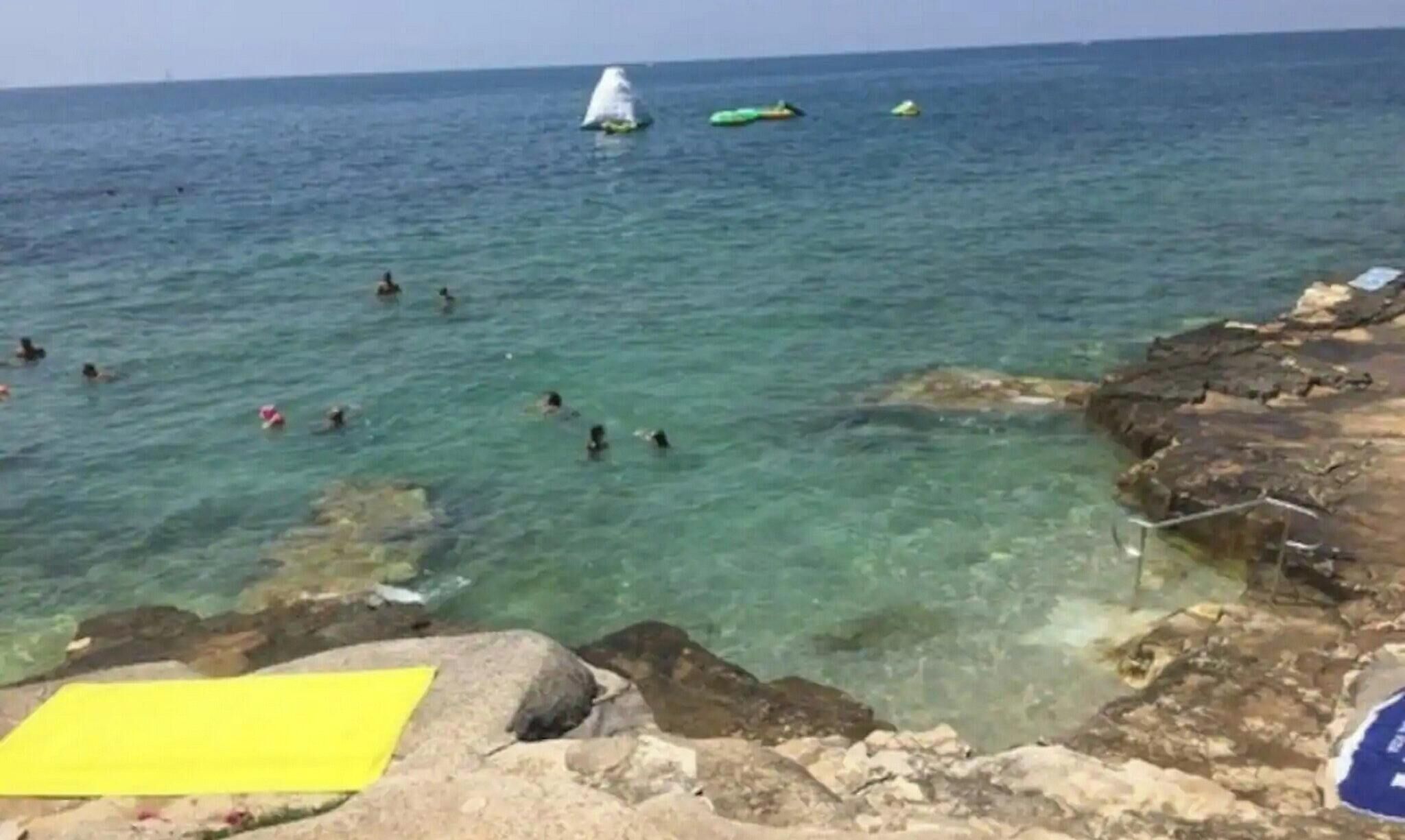 Uma costa rochosa com água cristalina e pessoas nadando.