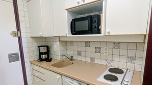 Een kleine keuken met witte kastjes, een magnetron, een koffiezetapparaat, een spoelbak en een Bosch vaatwasser.