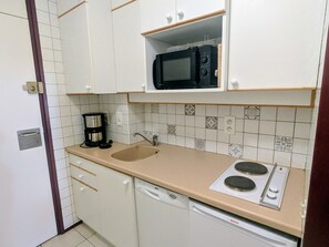 Een kleine keuken met witte kastjes, een magnetron, een koffiezetapparaat, een spoelbak en een Bosch vaatwasser.