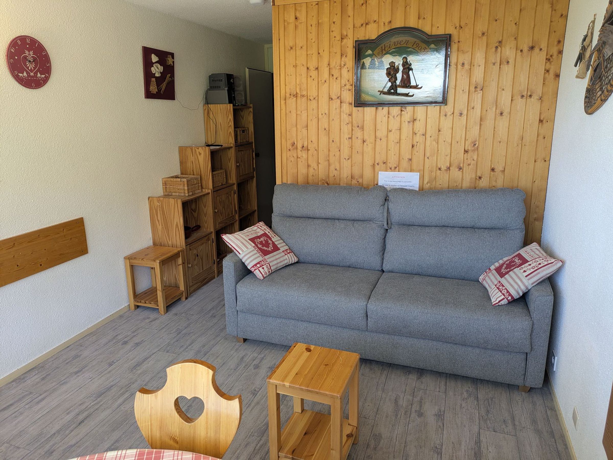 A cozy room with a grey sofa, wooden shelves, a small table, and a heart-shaped chair.