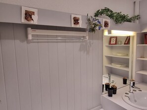 Een badkamer met een wit wastafelmeubel, een wastafel en een spiegel. Er hangen afbeeldingen in lijsten aan de muur en staat een plant boven de spiegel.