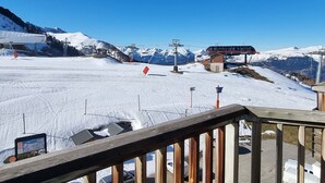 Een besneeuwde skipiste met een kabelbaan, een houten uitkijkpunt en een berg op de achtergrond.