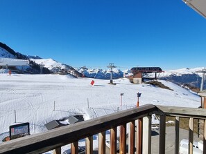 Een besneeuwde skipiste met een kabelbaan, een houten uitkijkpunt en een berg op de achtergrond.
