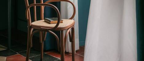 A chair with a woven seat and backrest, positioned in front of a window with white curtains.