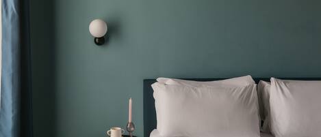 A neatly made bed with white linens, a bedside table with a book, a candle, and a small vase.