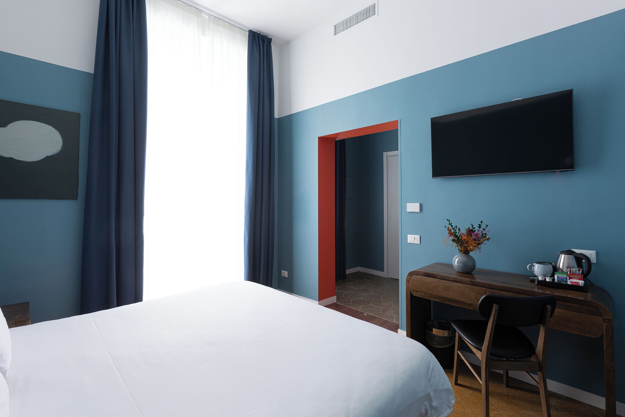 Habitación de hotel con cama, escritorio con silla, televisor de pantalla plana y un florero con flores.