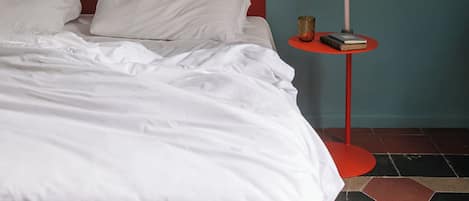 A neatly made bed with white bedding, a red headboard, and a small side table with a candle and a book.