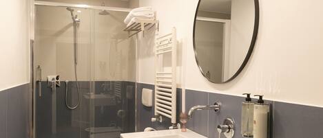 A modern bathroom with a glass-enclosed shower, a white sink, and a large mirror.
