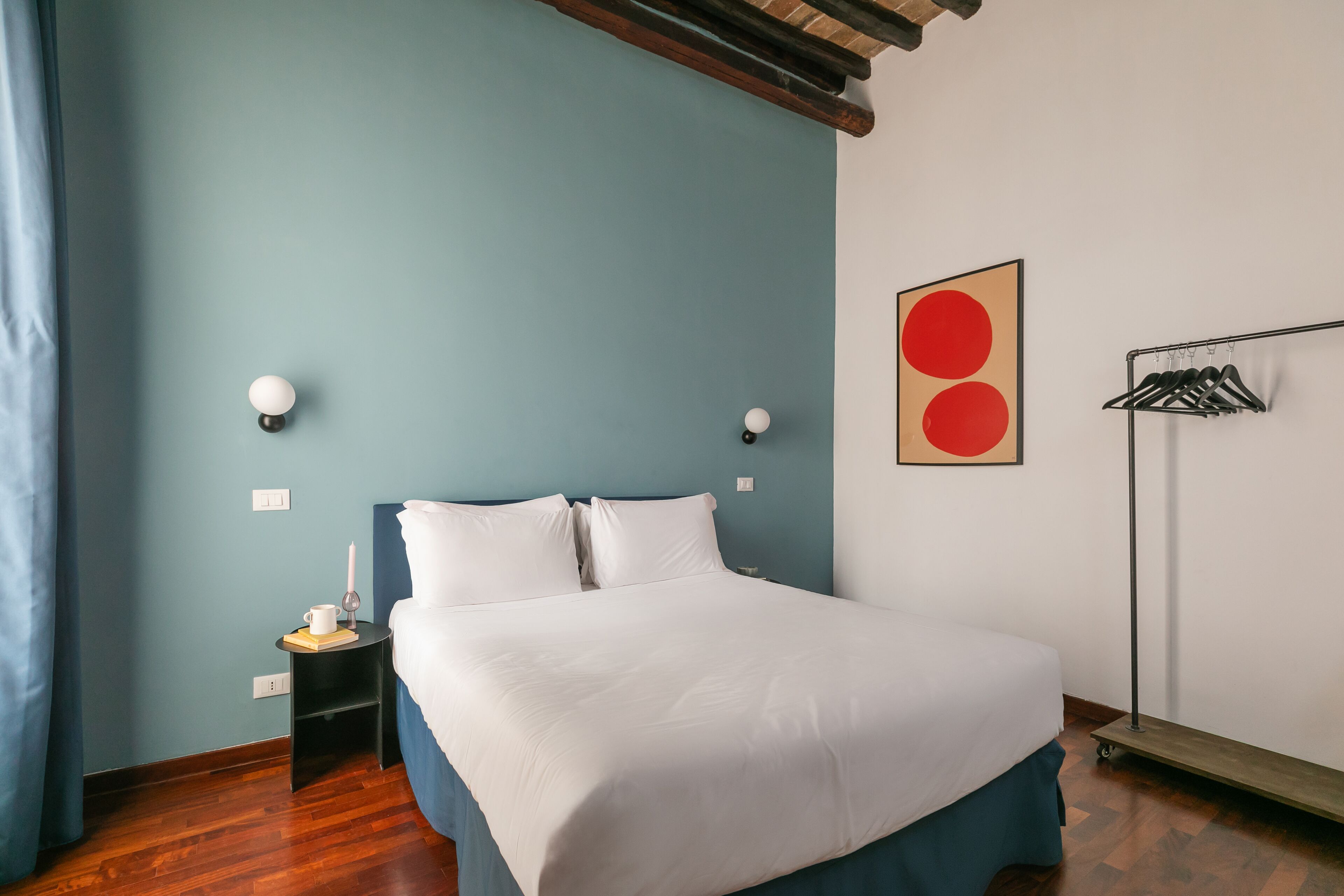 A bedroom with a bed, a nightstand, a wall-mounted lamp, and a coat rack.