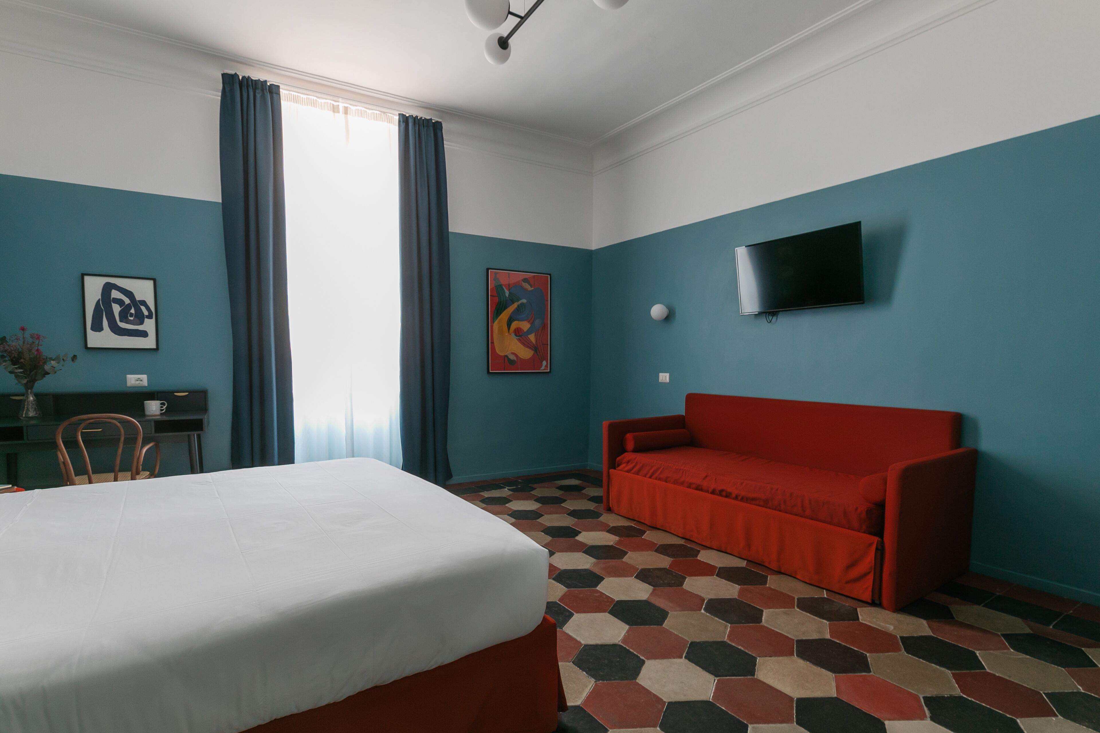 A hotel room with a bed, a red sofa, a TV, and a desk with a chair.