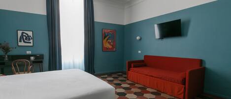 A hotel room with a bed, a red sofa, a TV, and a desk with a chair.