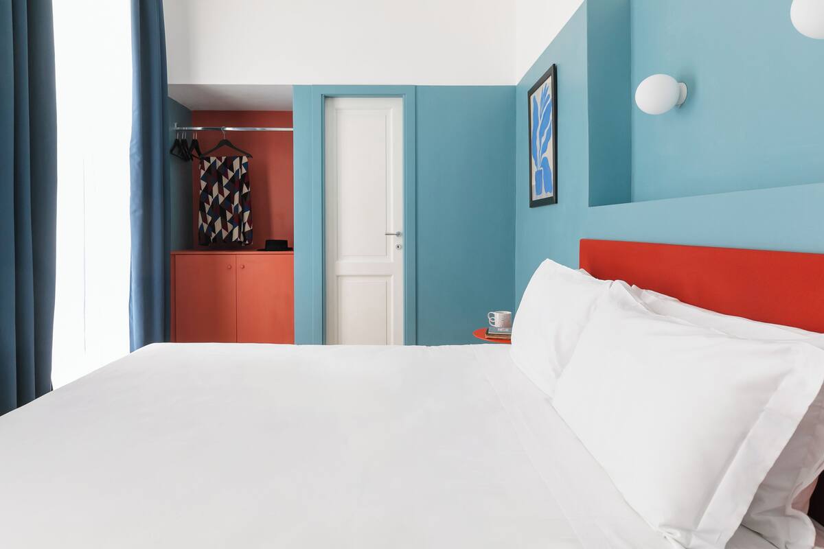 A hotel room with a large bed, a wardrobe, a door, and a wall-mounted light fixture.