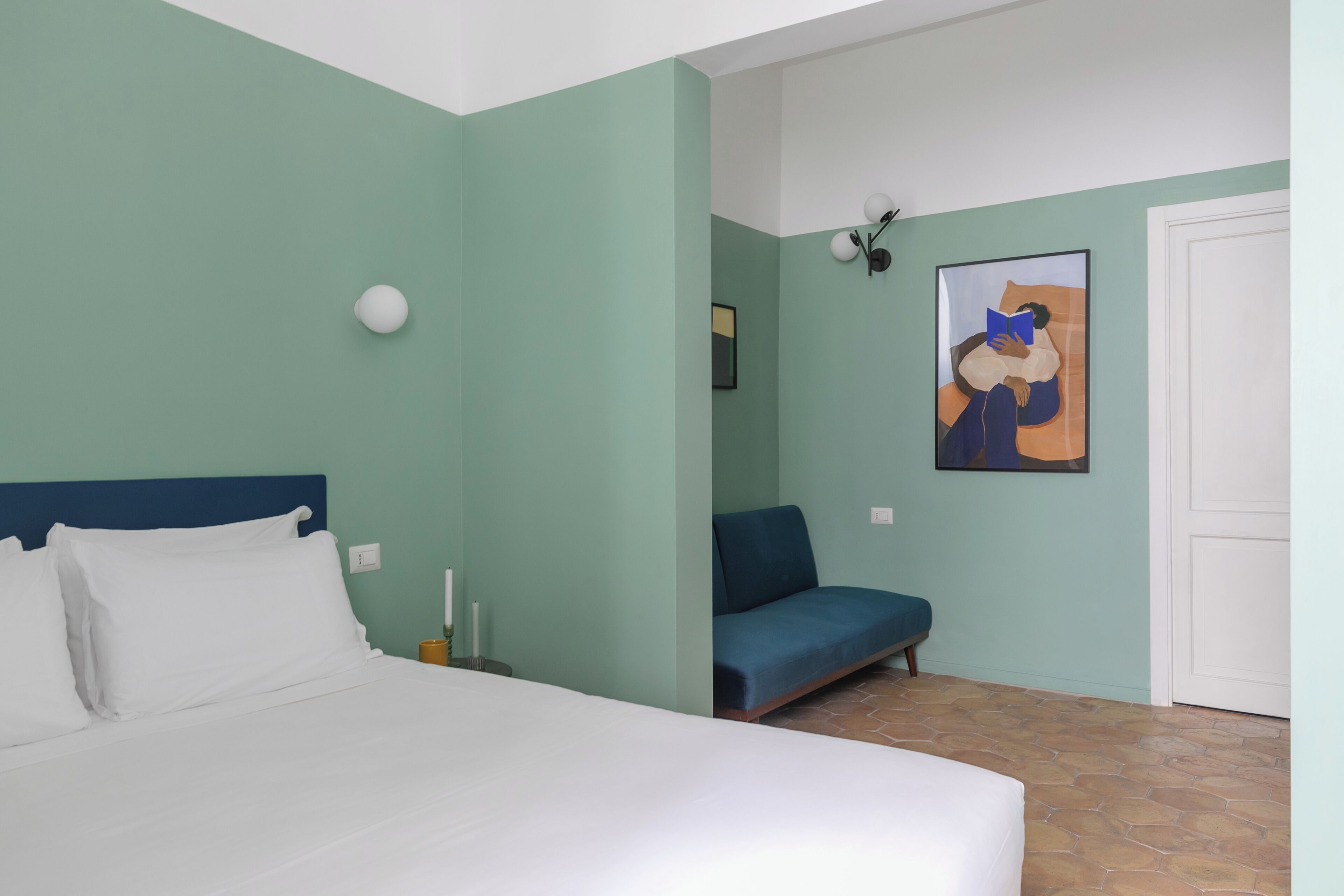 Un dormitorio con una cama, un sofá azul, un cuadro y una puerta blanca.