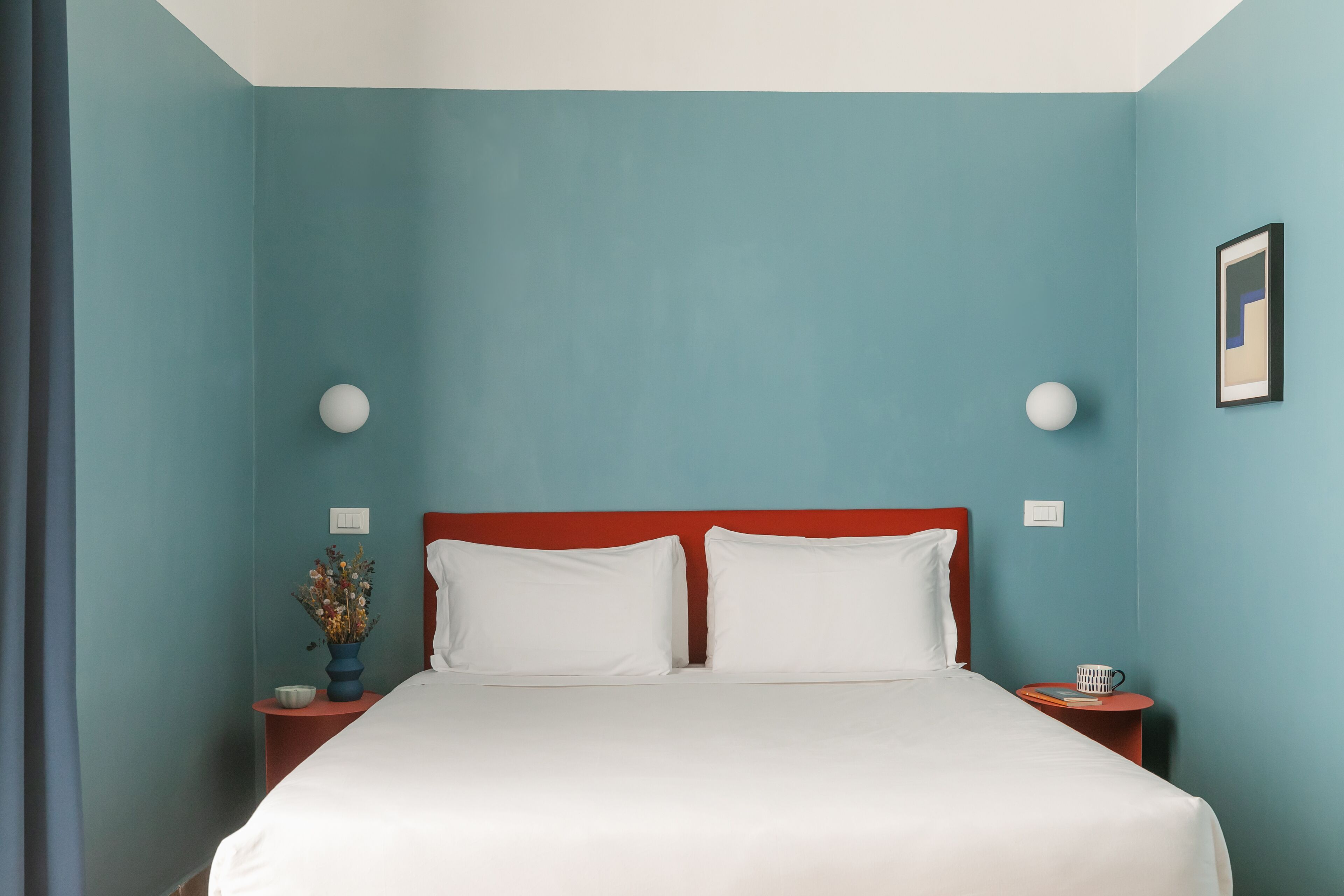 A neatly made bed with white linens, two white pillows, and a red headboard in a room with teal walls.