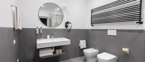 Un baño moderno con un lavabo blanco, un espejo redondo, un bidé y un perchero para toallas.