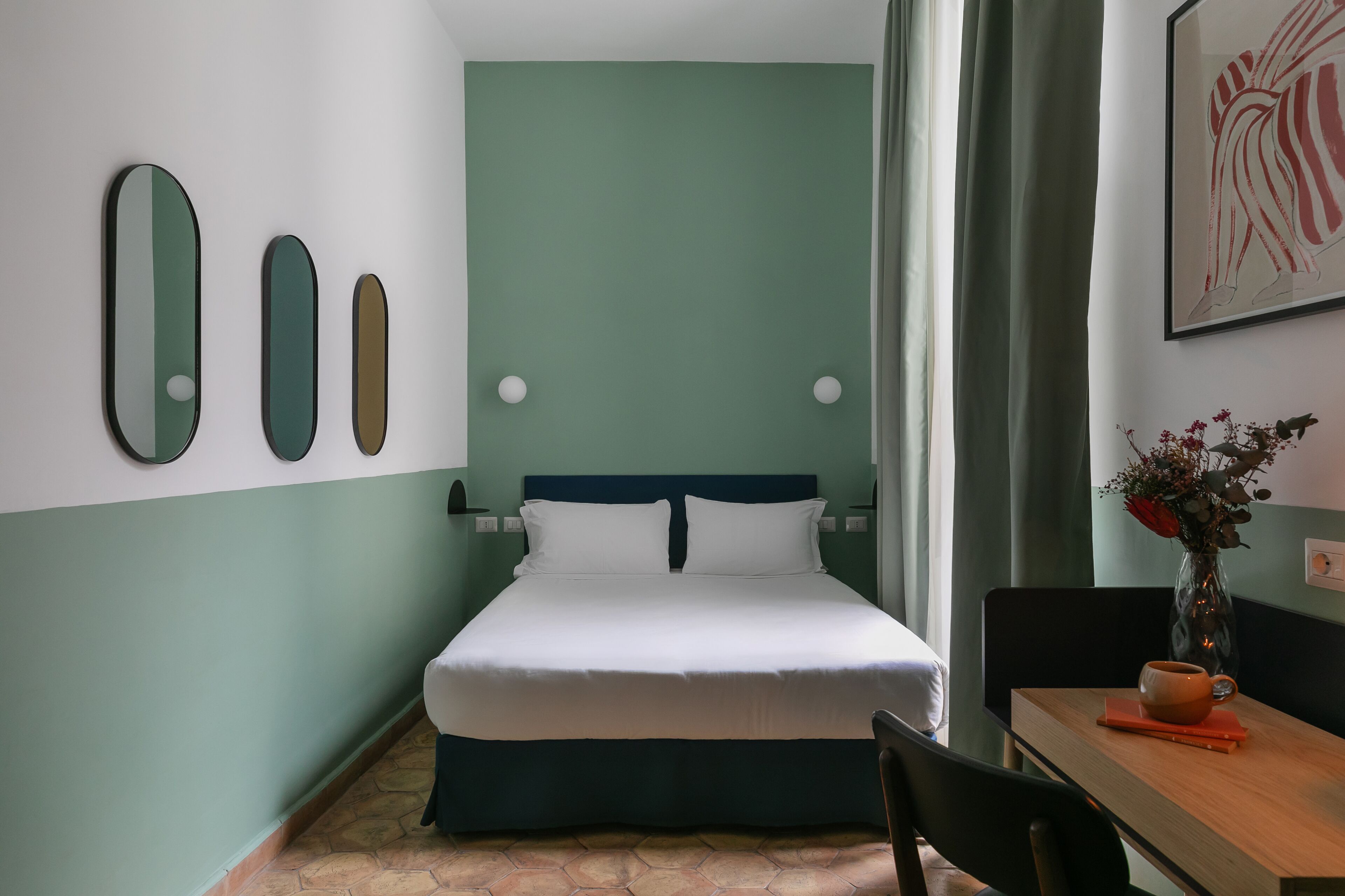A neatly arranged hotel room with a bed, a table with a vase of flowers, and wall art.