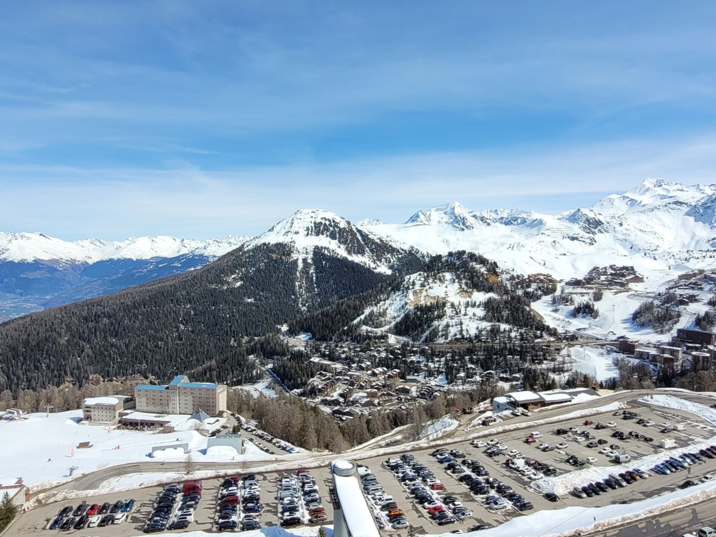 A mountainous town with a large parking lot and a prominent building with a blue roof.