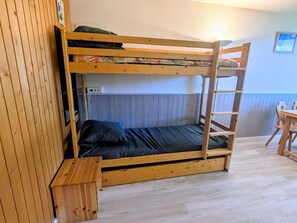 A bunk bed with a wooden frame, a small wooden table, and a wall-mounted electrical outlet.
