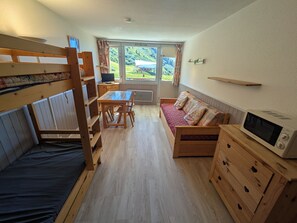 A compact room with a bunk bed, a sofa, a dining table, and a microwave.