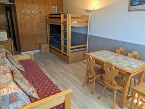 A wooden bunk bed with a desk and chair, a sofa with patterned cushions, and a dining table with chairs.