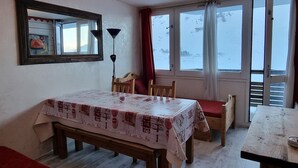 Une pièce avec une table et des chaises en bois, un banc, un miroir et une fenêtre avec des rideaux.