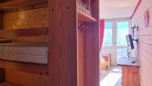 Une pièce en bois avec un lit superposé, un bureau avec un ordinateur et une fenêtre avec des rideaux.