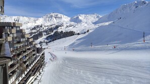 Une piste de ski enneigée, avec un bâtiment doté de balcons et un télésiège en arrière-plan.