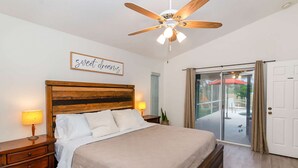 A bedroom with a wooden headboard, a bed with white bedding, two bedside lamps, a ceiling fan, and a sliding glass door leading to an outdoor area.