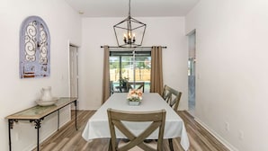 A dining area with a table set for four, a chandelier, and a view through a glass door.