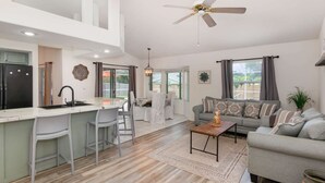 A modern kitchen with a central island, a dining area with chairs, a sofa, and a ceiling fan.