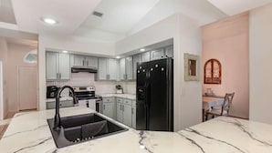 A modern kitchen with white cabinets, a black refrigerator, a sink with a black faucet, and a marble countertop.