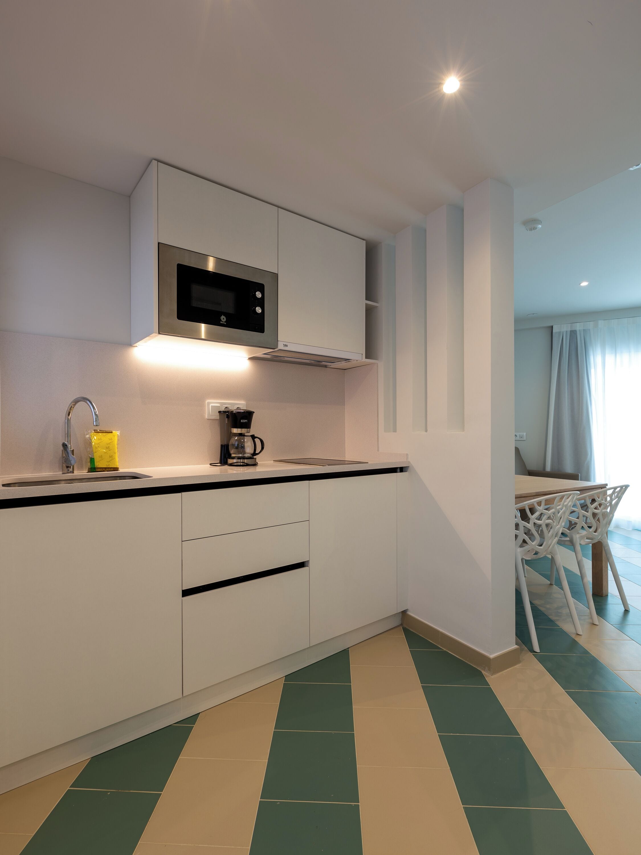 A modern kitchen with white cabinetry, a built-in microwave, and a coffee maker.