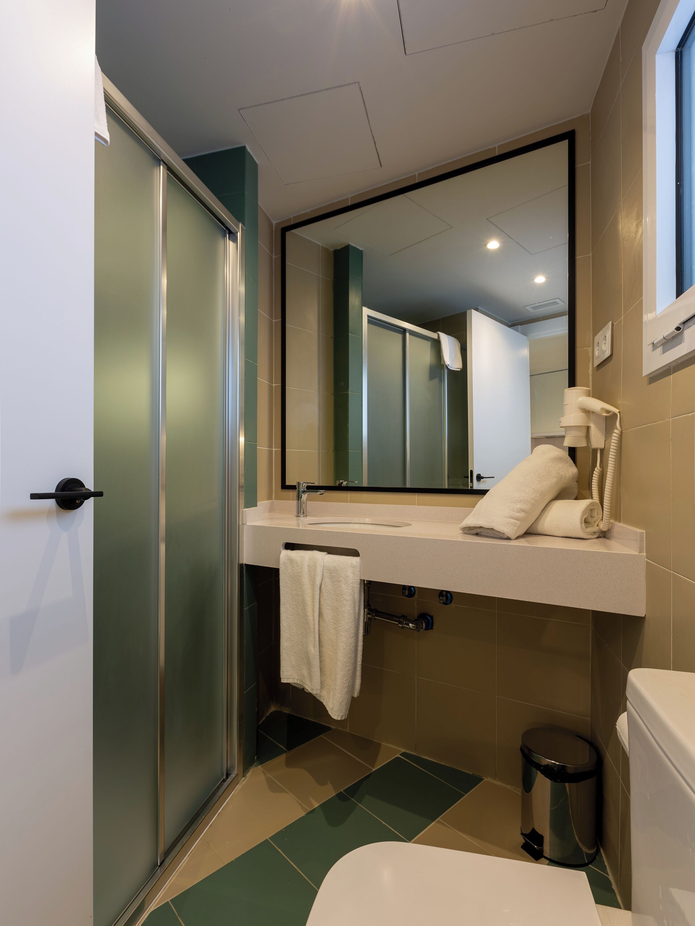 Un baño moderno con mampara de vidrio, lavamanos con toalla, espejo y retrete.
