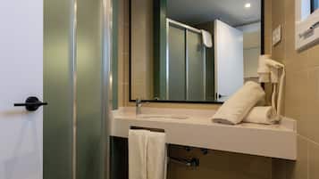Un baño moderno con mampara de vidrio, lavamanos con toalla, espejo y retrete.