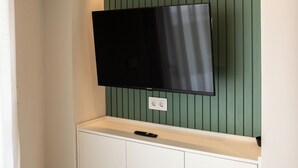 A flat-screen TV mounted on a wall with a green panel design. - SUNWAY ATLANTA (Sitges)