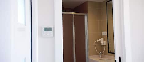 Un baño moderno con cabina de ducha de vidrio, panel de control en la pared y un espejo sobre el lavabo.