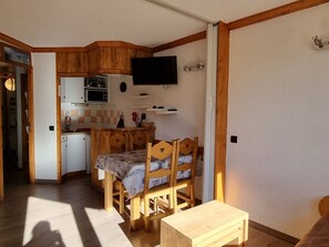 Una cocina compacta con armarios de madera, un microondas y un televisor montado sobre la encimera.