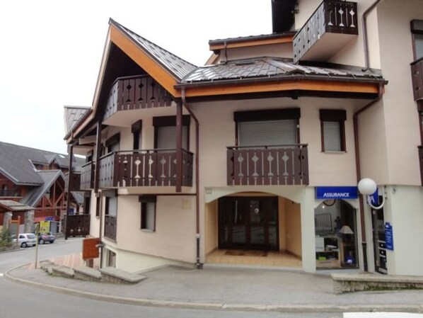 A two-story building with a balcony on the second floor, a storefront with an 'Assurance' sign, and a small entrance with a door.
