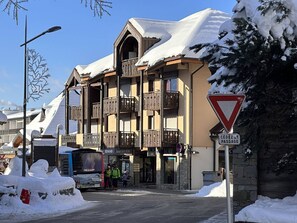 Un immeuble à plusieurs étages, doté de balcons, d’un toit enneigé et d’une enseigne indiquant un passage.