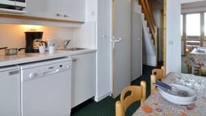 A compact kitchen with a microwave, coffee maker, sink, and dishwasher. A dining area with a table set for four and chairs is visible.