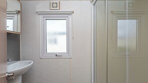 Ein Badezimmer mit einem weißen Waschbecken, einem Fenster und einer Duschkabine aus Glas.