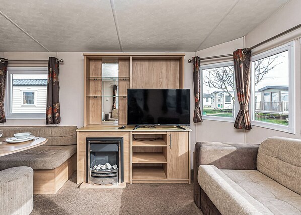 A modern RV interior with a flat-screen TV, wooden cabinetry, a fireplace, and a sofa.