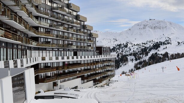 Un hotel de varios pisos con balcones y una pista de esquí al fondo.