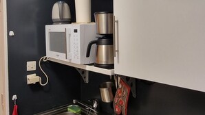 Una cocina con microondas, cafetera y hervidor sobre una estantería.