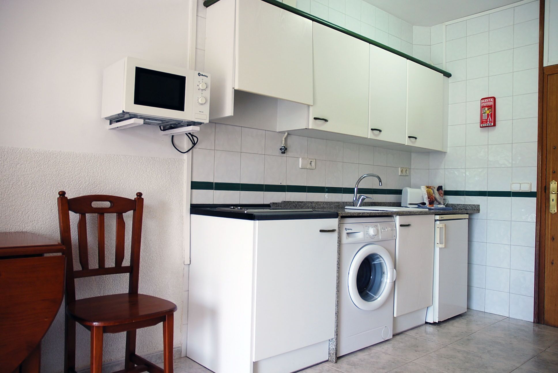 Cocina compacta con alacenas blancas, microondas, lavadora y pileta.